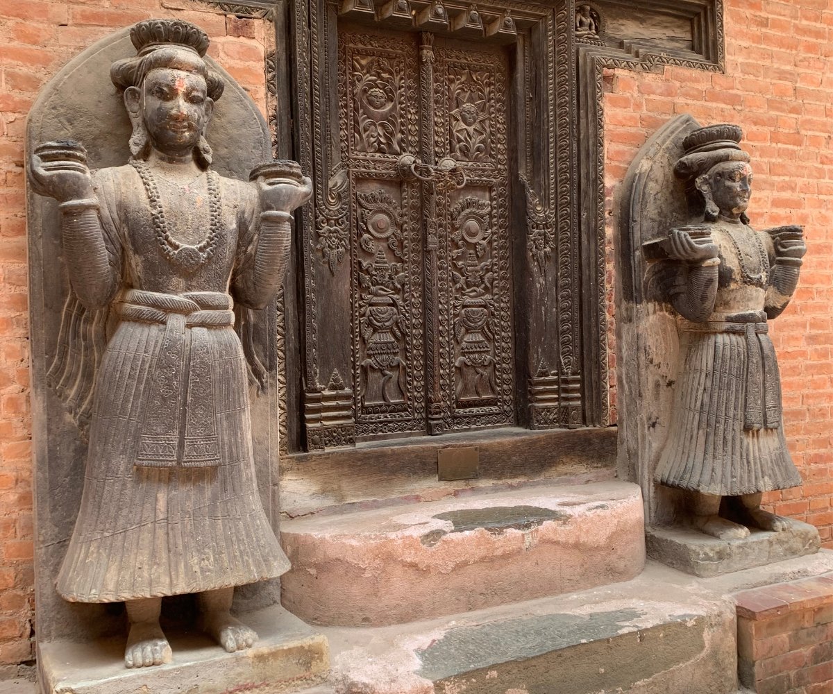 Stone guardian statues flanking an intricately carved wooden temple door in Bhaktapur, Nepal