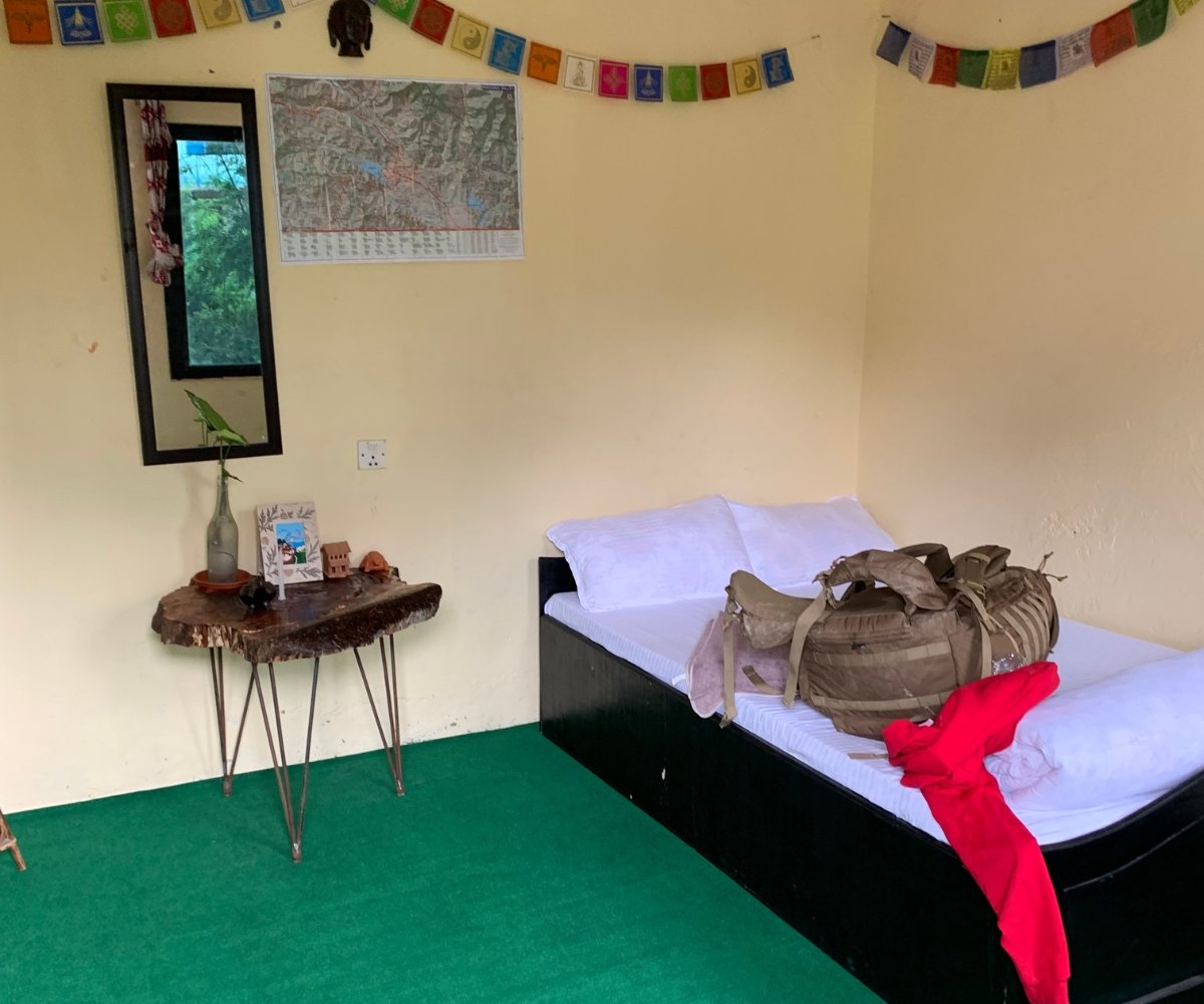 Simple guesthouse room in Pokhara with a single bed, prayer flags, and a rustic wooden table

