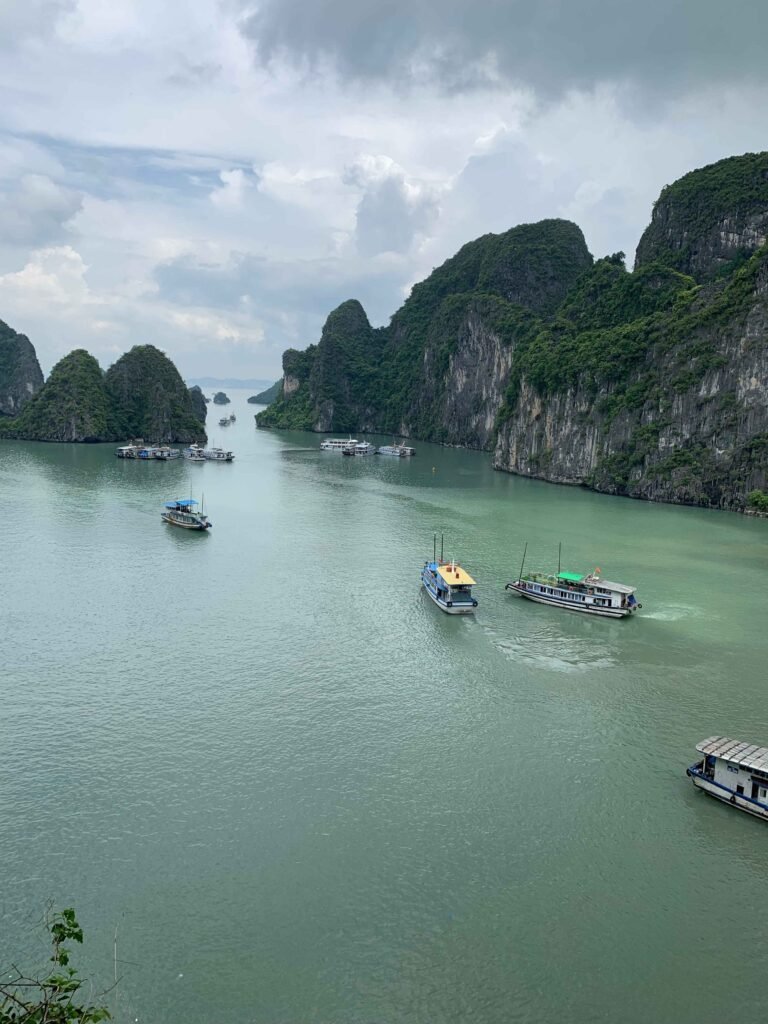 Boats cruising through the emerald waters of Ha Long Bay, surrounded by cliffs.
