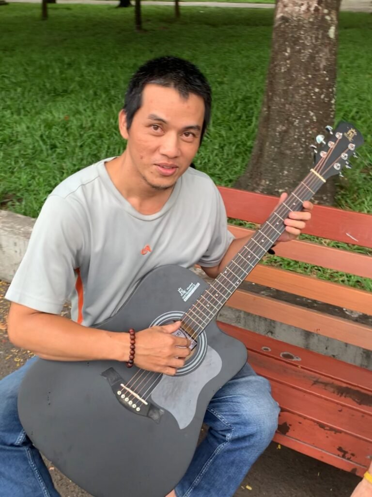 Foong playing a black acoustic guitar on a park bench in Vietnam