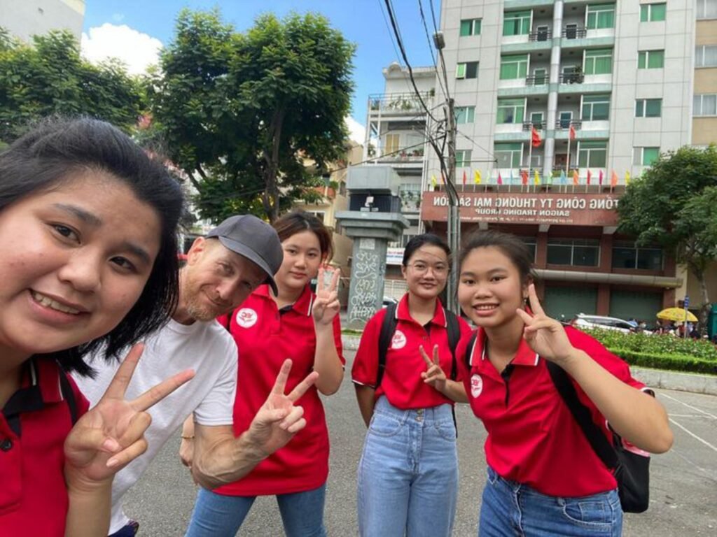 Smiling Vietnamese students and a tourist pose for a photo in front of the Saigon Training Group building
