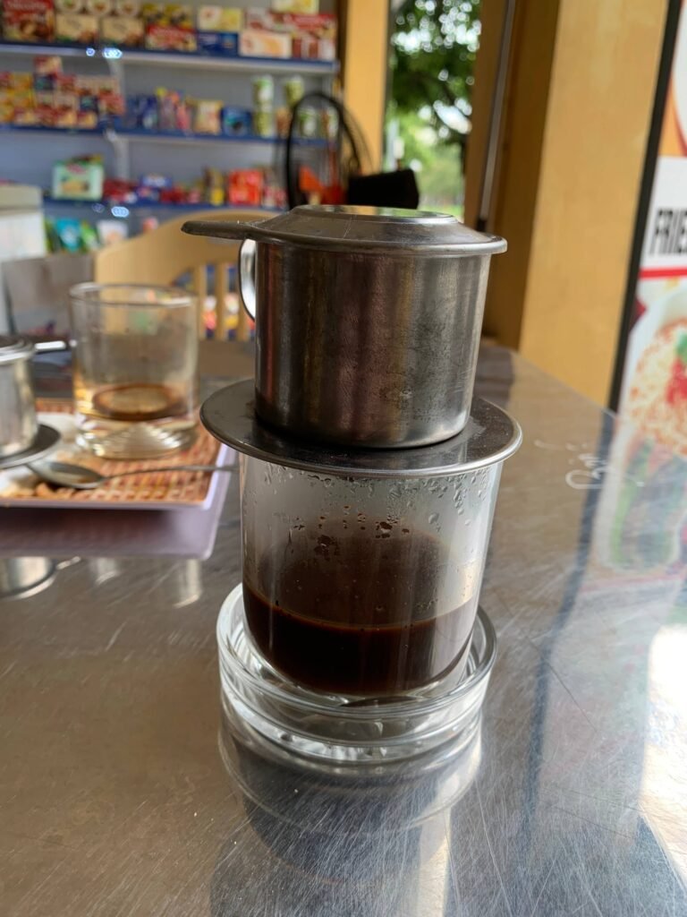 A close-up of Vietnamese drip coffee brewing in a traditional metal phin filter.
