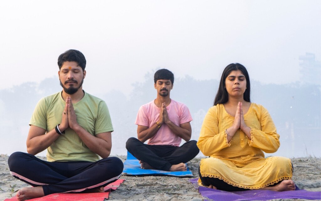 group-yoga-meditation-outdoors Three yoga students meditating outdoors in seated prayer pose.