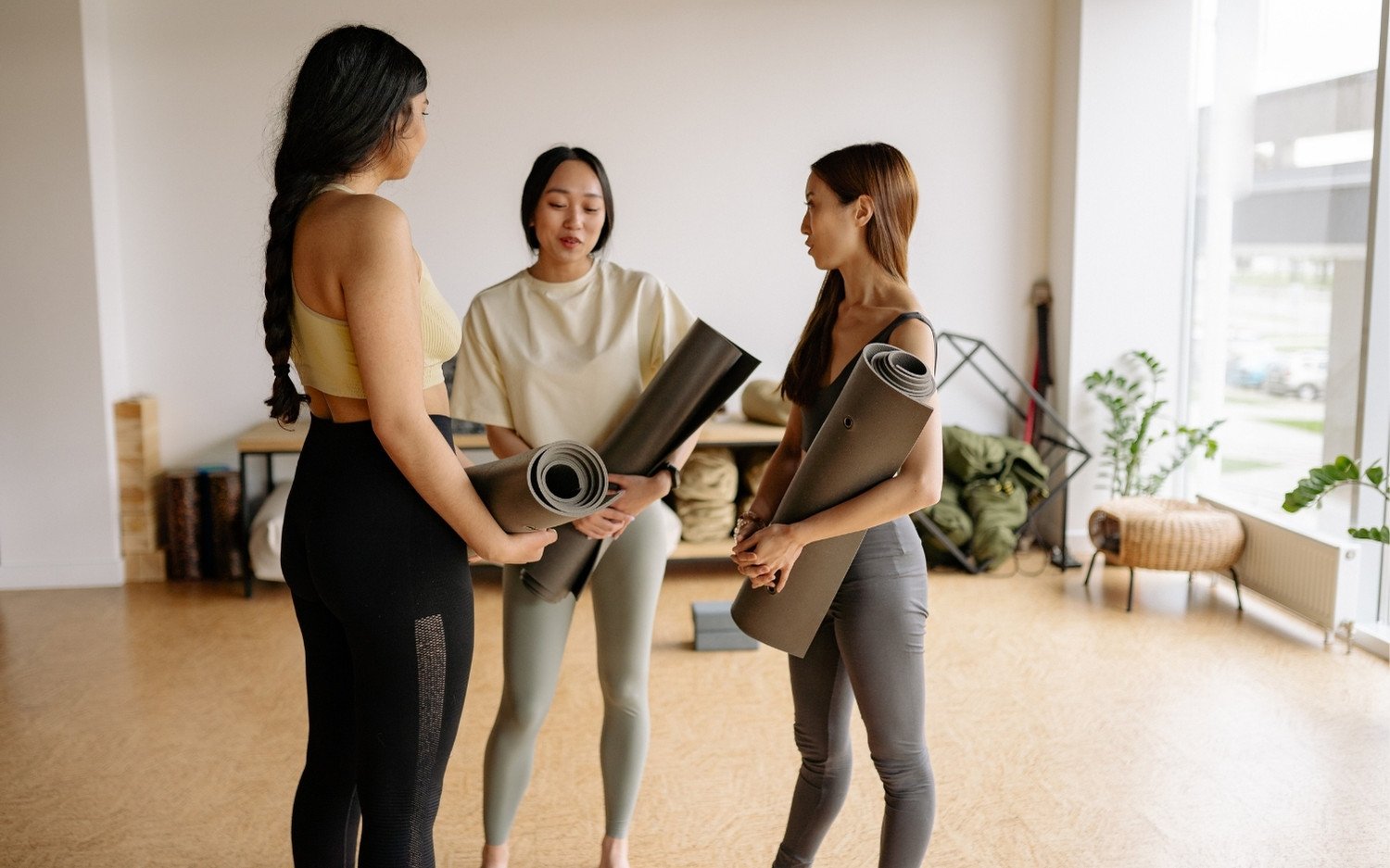 Three women holding yoga mats and talking before class
