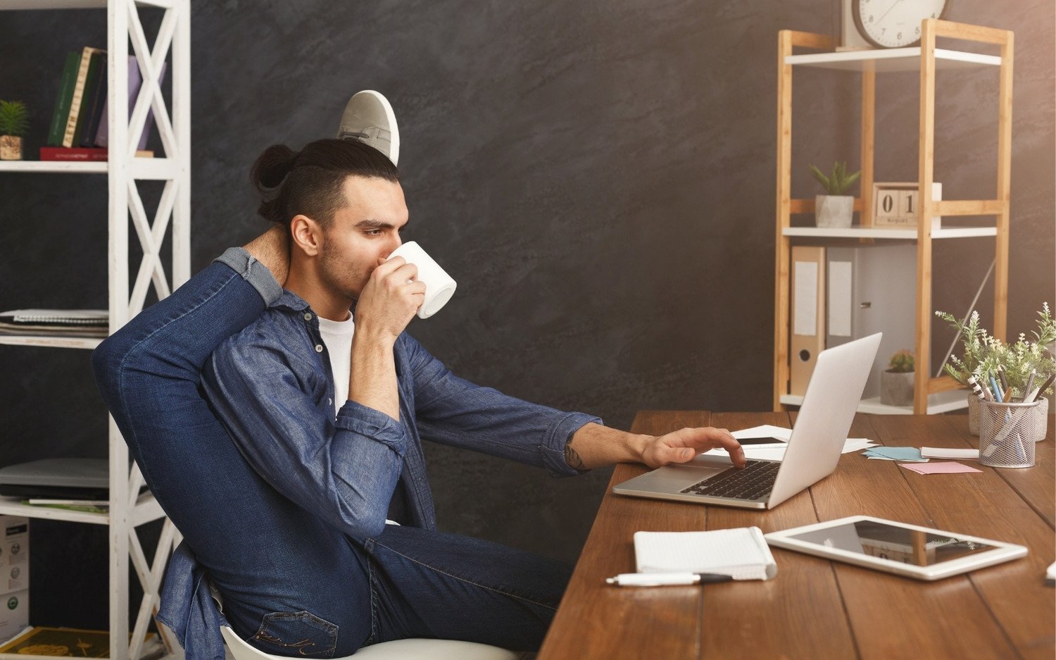 Man practicing yoga pose while working at desk with laptop while looking at yoga teacher training options online