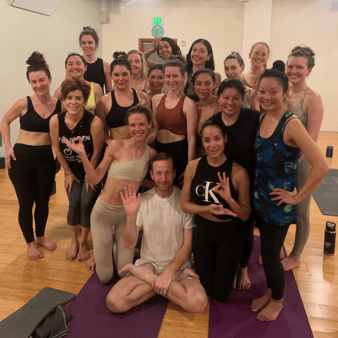 Group of yoga teacher training graduates smiling and posing together in a yoga studio.