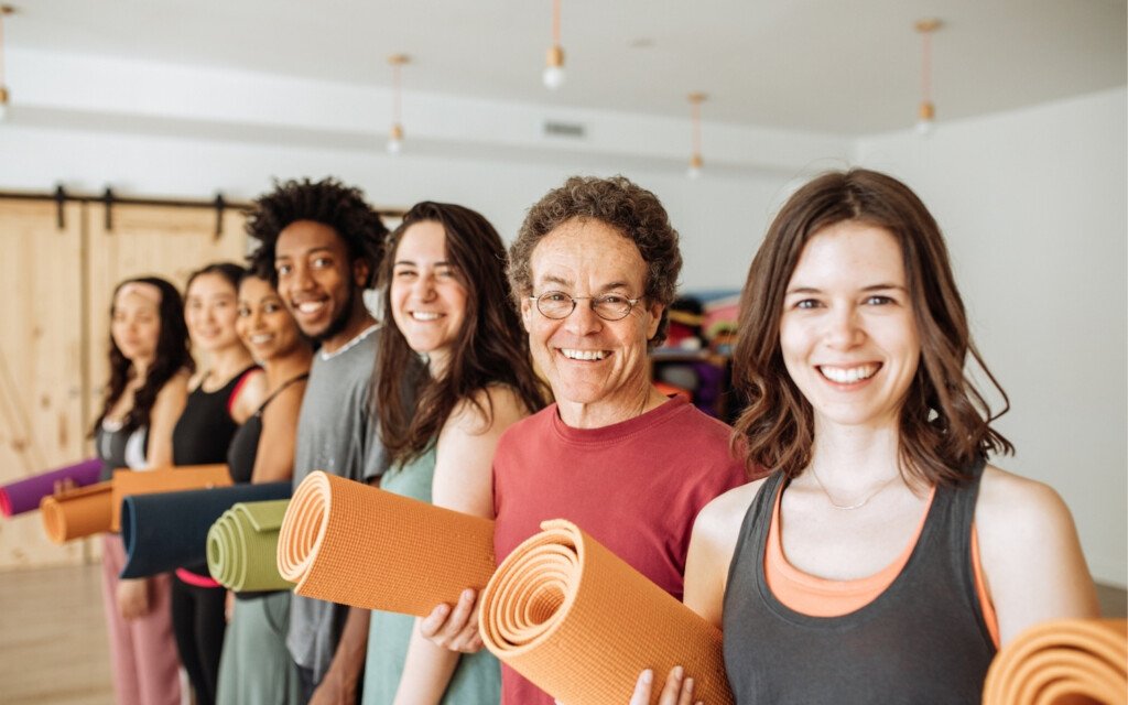 yoga-teacher-training-group-ready Group of smiling yoga students holding mats in a studio