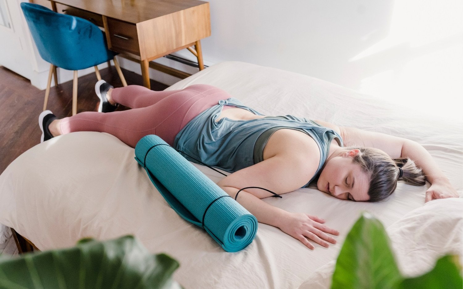 Yoga trainee resting face-down on bed with yoga mat after long training day