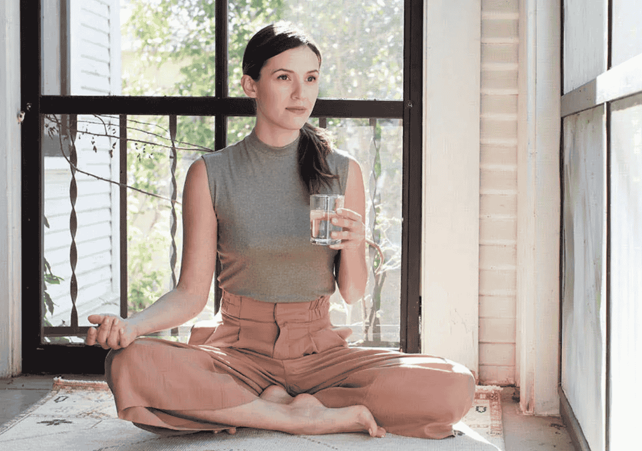 Adriene Mishler sitting cross-legged with a glass of water, calm and mindful