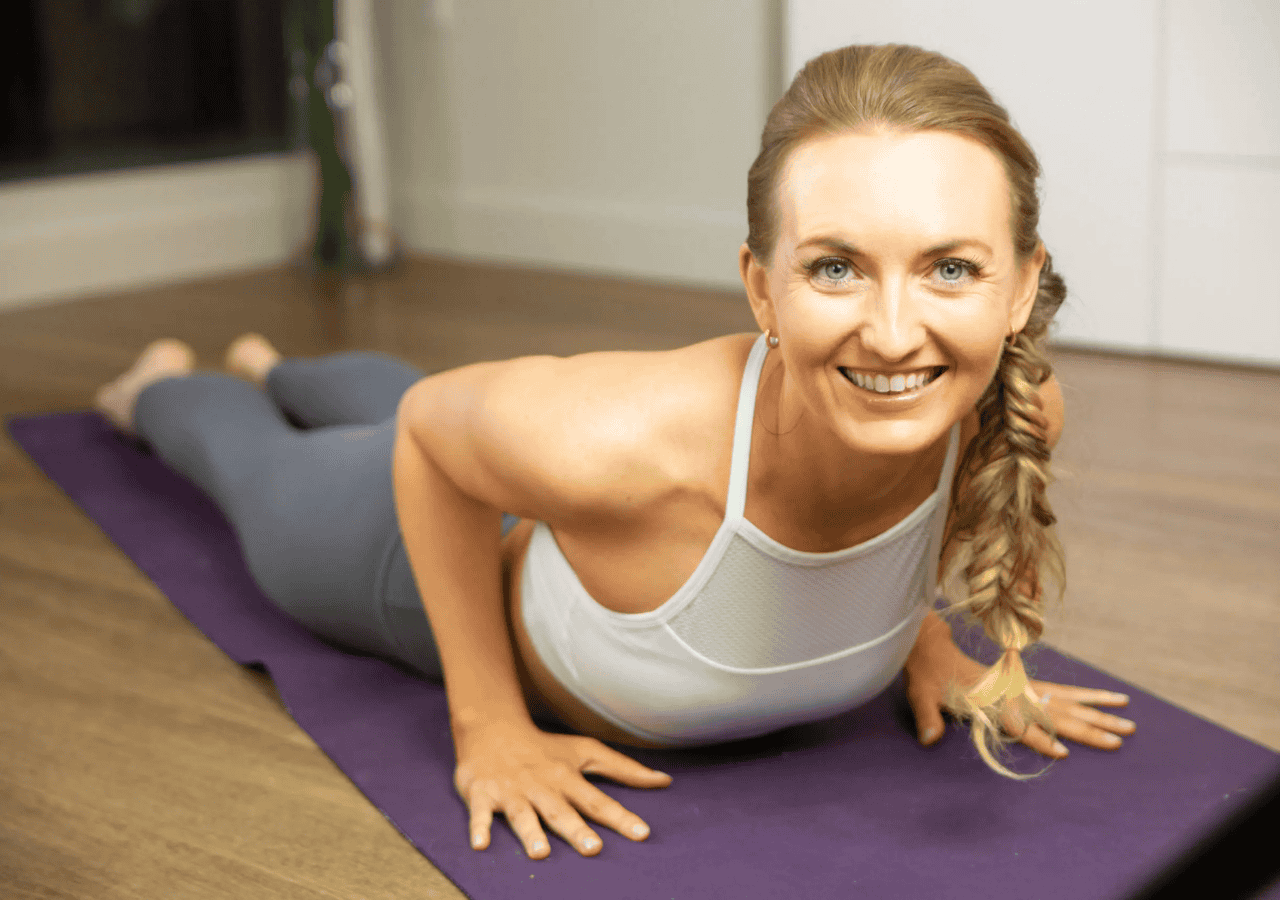 Brett Larkin smiling in upward-facing dog pose on a yoga mat