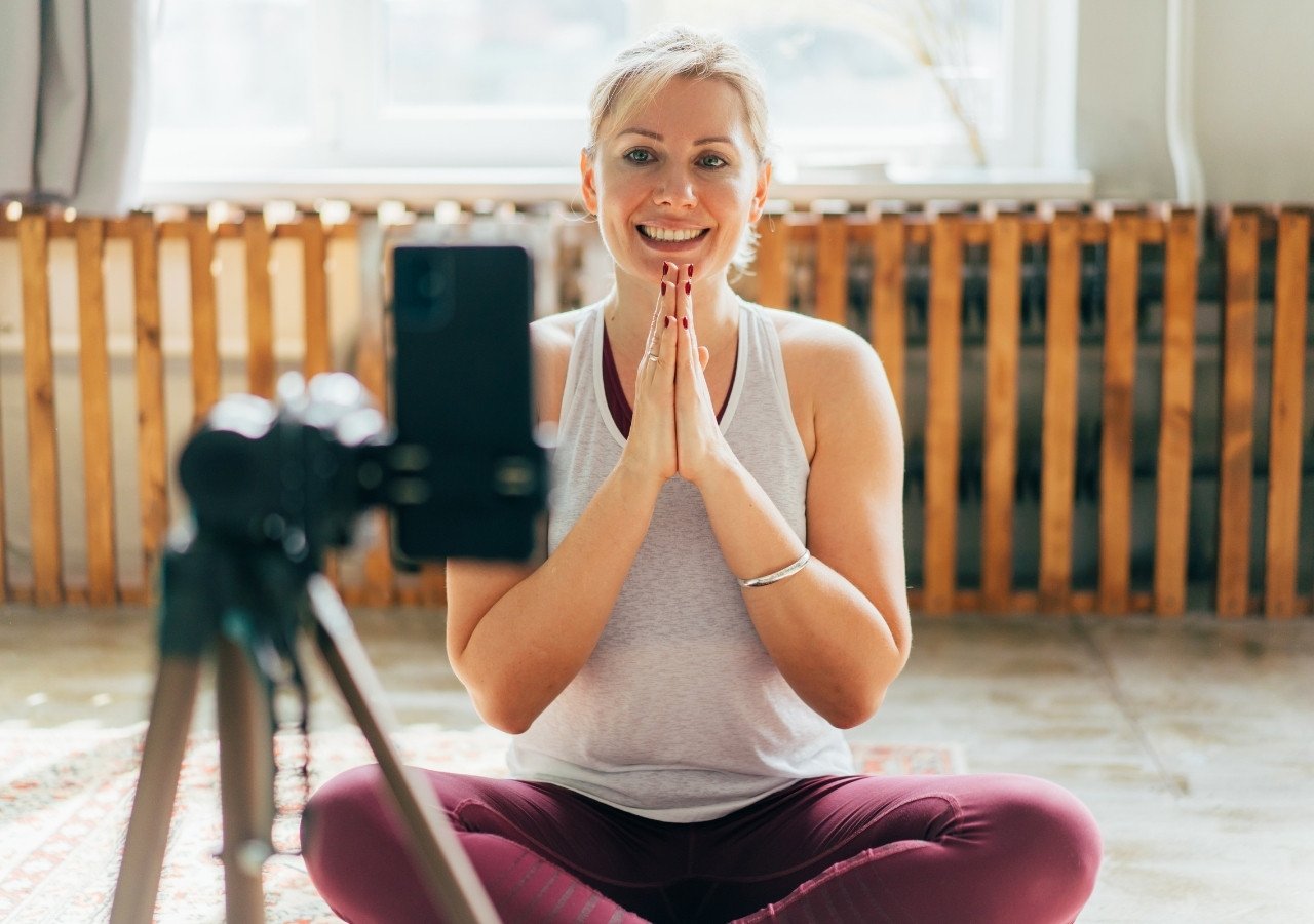 Smiling yoga teacher greeting students while recording an online yoga class