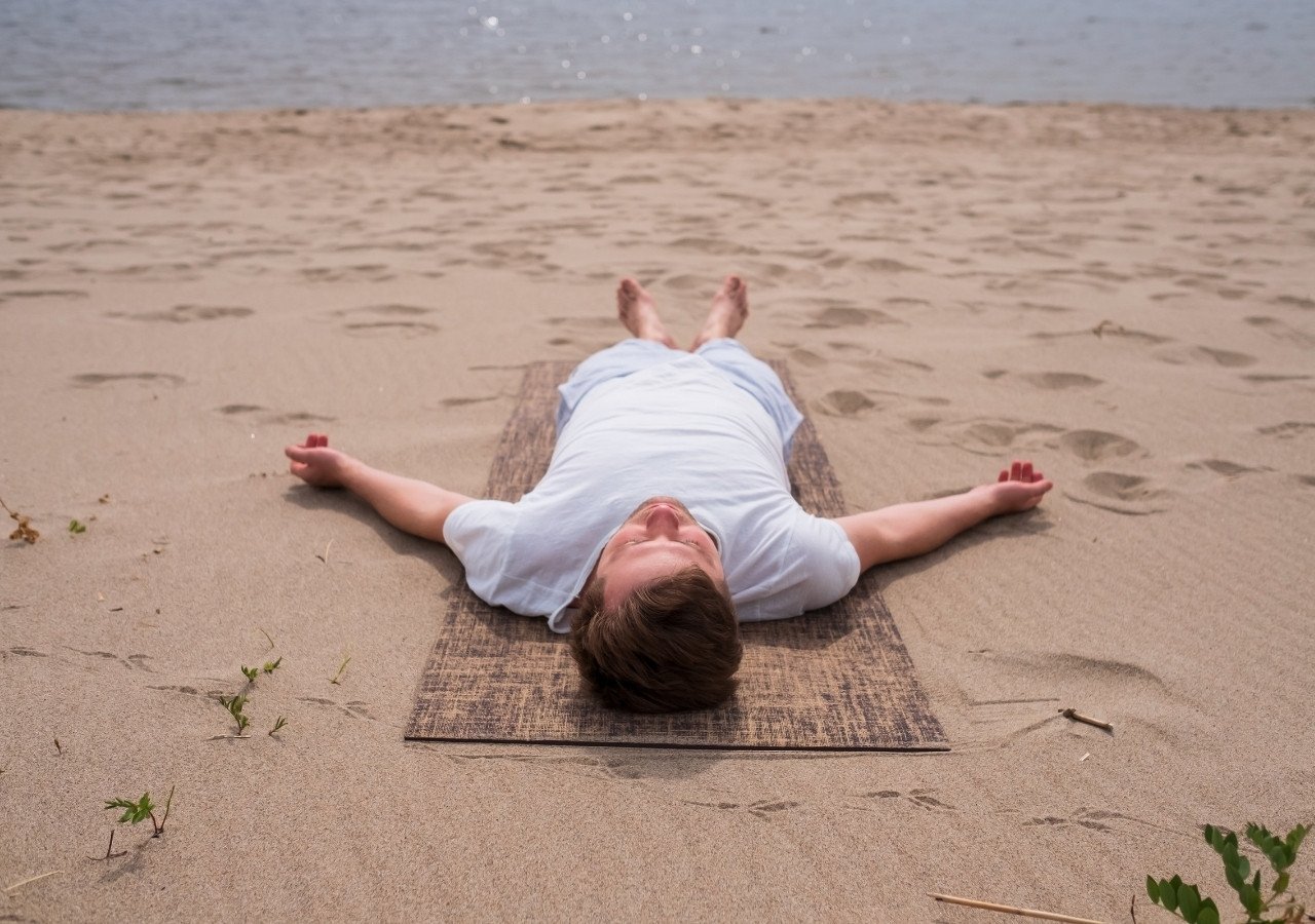 Man practicing Yoga Nidra in savasana pose on the beach