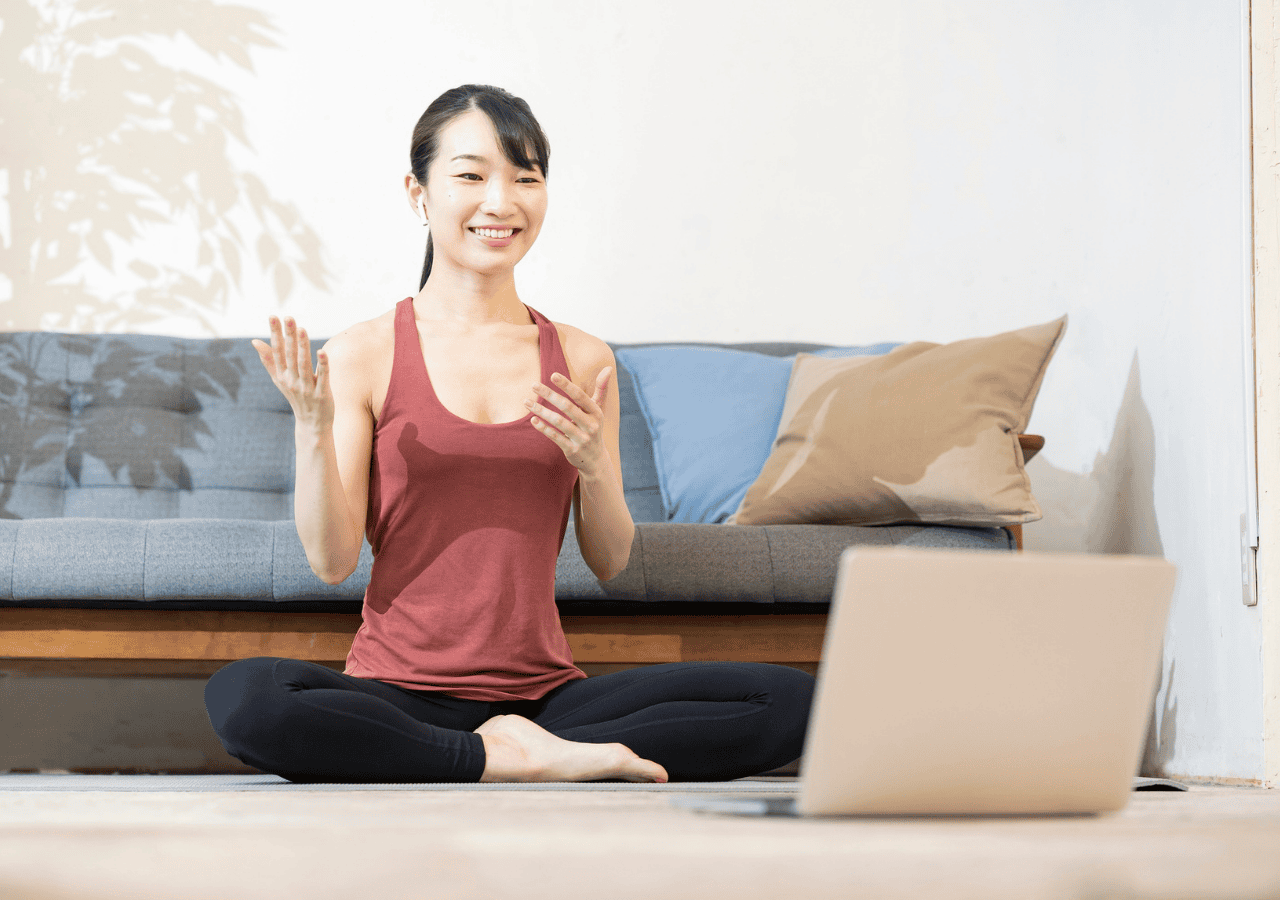 Yoga teacher smiling and teaching an online yoga class through a laptop
